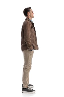 Deri ceketli rahat akıllı adam beyaz arka planda ceplerini tutarken sırada bekliyor.