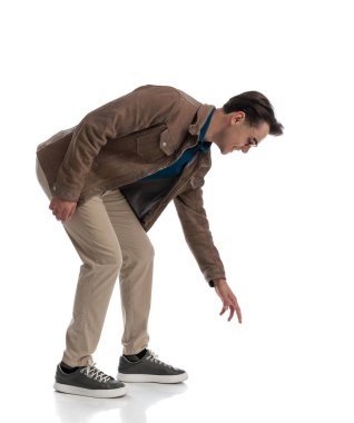 Meraklı, zeki, sıradan bir adam beyaz arka planda dururken yerden bir şey almak için eğiliyor.