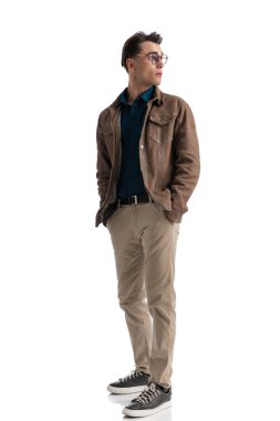 Kahverengi deri ceketli rahat, rahat ve rahat bir adam. Elinde cepleri olan, beyaz arka planda duran, tüm vücudunu gösteren bir adam.
