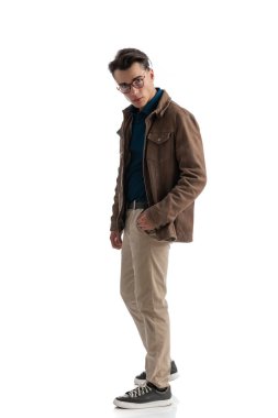 Beyaz arka planda duran, baştan çıkarıcı görünen, ceplerini tutan seksi, zeki, sıradan bir adamın yan görüntüsü.