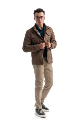 Kahverengi deri ceketinin düğmelerini ilikleyen yakışıklı genç bir adam beyaz arka planda dikiliyordu.