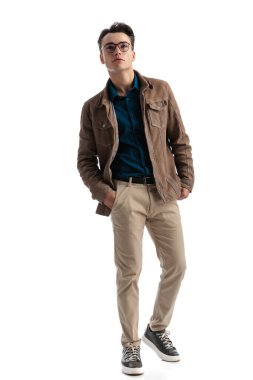 Ceplerini tutan ve beyaz arka planda öne doğru adım atan seksi, zeki, sıradan bir adam.