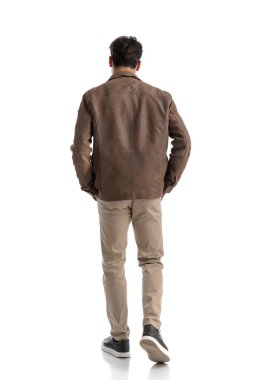 Arkaya bakan rahat moda adamı beyaz arka planda yürürken, cepleri tutarken, tüm vücudunu gösteriyor.