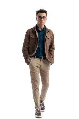 Deri ceket ve gözlük takmış, beyaz arka planda rahatça yürüyen seksi bir genç adam.