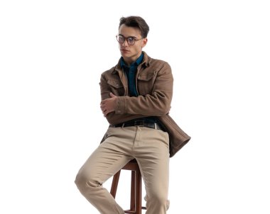 Deri ceketli, gözlüklü, kolları bağlı beyaz arka plana bakan öğrencilerin yakın çekimi.