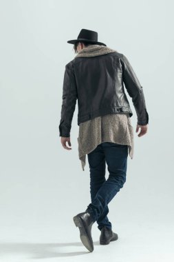 Şapkalı, gözlüklü, gri arka planda yürüyen ve aşağı bakan havalı motosikletli adamın manzarası.