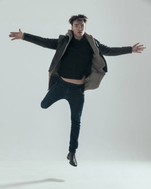 Havaya atlayan havalı genç adam ve gri arka planda özgürlüğü kucaklamak için kollarını açıyor.