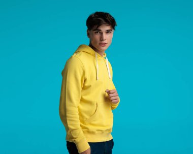 Yakından bakınca sarı kapüşonlu, yumruklu, kot pantolonunun cebini tutan, mavi arka planda yalnız gezen yakışıklı bir adam görüyorum.