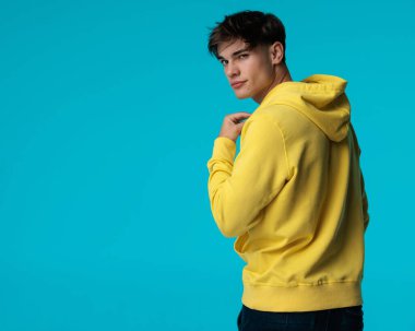 Baştan çıkarıcı genç adamın, mavi arka planda izole edilmiş sarı kapüşonlusunu yerleştirirken başını çevirmesine yakın plan.