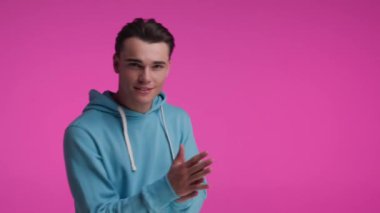 Mavi kazaklı seksi adam avuçlarını birbirine sürterek onu pembe arka planda takip etmeni istiyor.