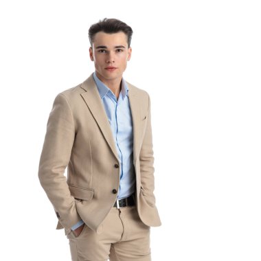 Bej takım elbiseli, mavi gömlekli, cebinde beyaz arka planda tek başına duran genç ve rahat bir adamın fotoğrafını çek.