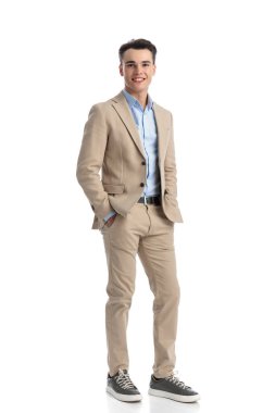 Beyaz arka planda duran, ceplerini tutan, tüm vücudunu gösteren rahat ve rahat bir adam.