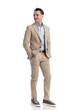 Rahat, rahat, rahat, takım elbiseli, gömlekli, gülümseyen ve ellerini cebine sokup beyaz arka planda dikilen bir adam.