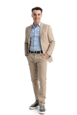 Beyaz arka planda durup gülümseyen bej takım elbiseli çekici bir öğrenci.
