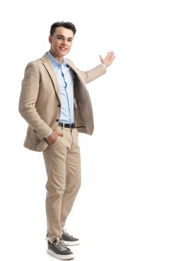 Rahat iş adamı bej takım elbiseli ve mavi gömlekli, elleri cebinde dururken yan yana duruyor.