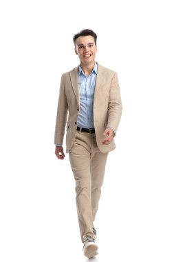 Bej takım elbiseli yakışıklı bir öğrenci ve mavi gömlekli beyaz arka planda yürüyor.