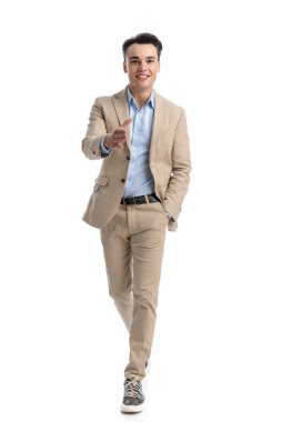 Bej takım elbiseli rahat bir işletme öğrencisi beyaz arka planda yürüyor ve el sıkışıyor.