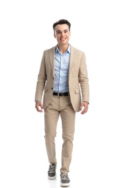 Bej takım elbiseli yakışıklı bir öğrenci gülümsüyor ve beyaz arka planda ileri adım atıyor.