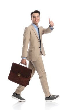 Mutlu iş adamı, beyaz arka planda yürürken ve evrak çantasını tutarken tamam işareti yapıyor.