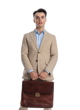 Bej takım elbiseli genç işletme öğrencisinin beyaz arka planda dururken elinde evrak çantasıyla önünü kapatın.