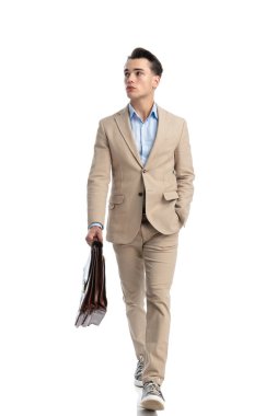 Bej takım elbiseli ve elinde bavulla beyaz arka planda yürüyen rahat iş adamı