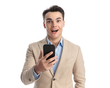 Beyaz arka planda mutlu görünürken cep telefonuna mesaj yazan şaşırmış, sıradan bir adamın yakın plan fotoğrafı.