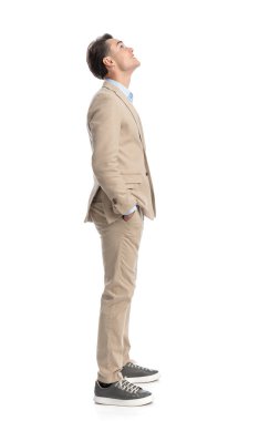 Bej takım elbiseli rahat iş adamının beyaz arka planda dikilirken tüm vücudunu gösteren bir yan görünüm.