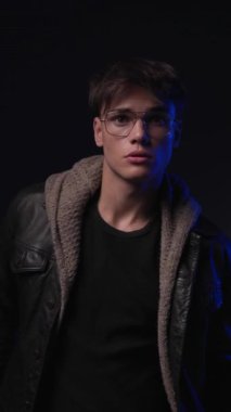 Gözlüklü mutlu genç adam kameraya bakıyor, aşağı bakıyor ve gülümsüyor.