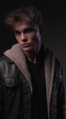 20 'li yaşlarda kendine güvenen genç bir adam. Çenesine dokunup düşünüyor. Avuçlarını ovuyor ve gri arka plana bakıyor.