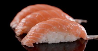 Üç parça Japon yemeği. Suşi denen pirinç ve somondan yapılmış. Siyah arka planda tek başına dönüyorlar.