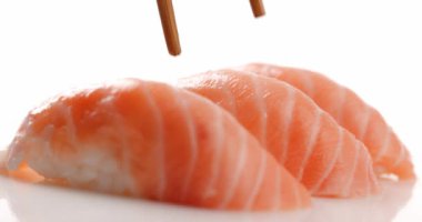 Taze somon nigiri suşisi yemeye hazır ve beyaz arka planda izole edilmiş yemek çubuklarıyla toplanmış.