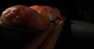 Japon mutfağının tadını çıkarın. Nigiri suşili, pembe somonlu ve siyah arka planda çubuklu karides.