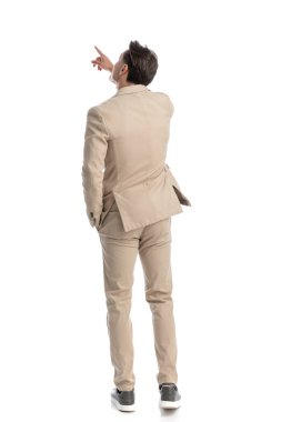 bej takım elbiseli rahat ve rahat bir adamın arkasında beyaz arka planda dikilirken parmaklarını sağa sola doğru gösteriyor.