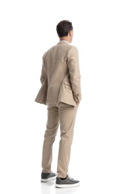 Bej takım elbiseli rahat ve rahat bir adamın beyaz arka planda dikilirken yan yana baktığı arka plan.