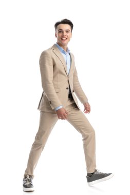 happy smart casual man wearing beige suit and blue shirt taking a wide step to the side, full body picture clipart