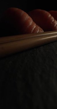 Çiğ somon ve yumuşak pirinçli taze nigiri suşisinin dikey videosunu kapatıyoruz. Siyah arka planda ahşap çubuklarla servis edilen tabakta mükemmel bir şekilde servis ediliyor.