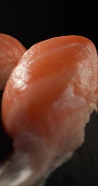 Kamera somon suşisi ve yemek çubukları etrafında dönüyor. Koyu arkaplandaki gri kaya masasında servis ediliyor.