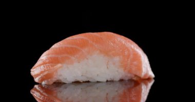 Bir parça somon nigiri sushi siyah arkaplanda izole haldeyken dönüyor