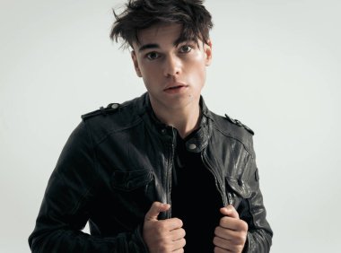 Gri arka planda duran deri ceketli seksi motorcunun portresi.