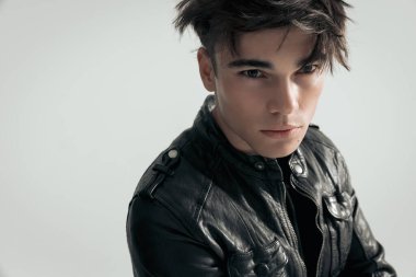Gri arka planda siyah deri ceketli seksi genç adama yaklaş.