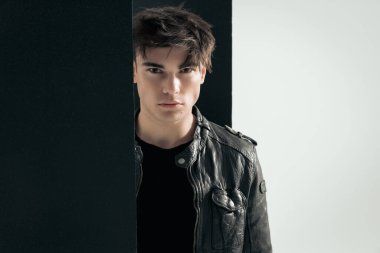 Siyah deri ceketli, siyah beyaz arka planda duran yakışıklı motorcunun yakın çekimi.