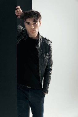 Gri arka planda siyah panele yaslanan deri ceketli seksi motosikletlinin yakın çekimi.