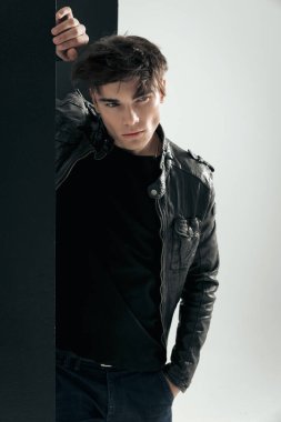 Gri arka planda siyah paneli tutarken yan yan bakan deri ceketli baştan çıkarıcı genç motorcunun yakın çekimi.