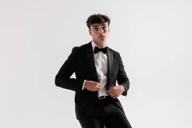 Gri arka planda otururken siyah takımının düğmelerini ilikleyen genç modacının yakın çekimi.