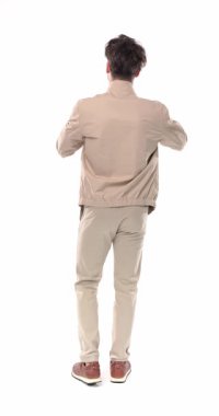 Seksi genç adam kameranın önünde duruyor, bej ceketini ayarlıyor, beyaz arka planda el ele tutuşup el ele tutuşuyor.