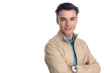 Bej ceketli seksi bir adamın portresi. Kollarını kavuşturup stüdyoda beyaz arka planda gülümsüyor.