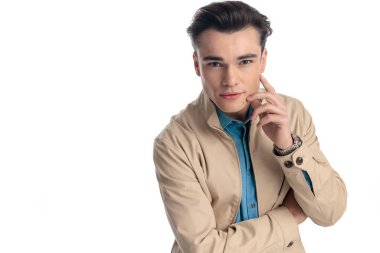 Bej ceketli, yanağına dokunan, beyaz arkaplan önünde ileriyi düşünen, ileriye bakan, düşünceli bir adam.