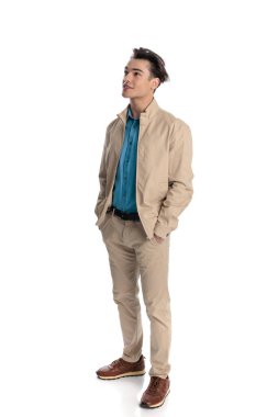 Bej ceketli mutlu adam elleri ceplerinde, yukarı bakıyor, gülümsüyor ve beyaz arka planda geleceği hayal ediyor.
