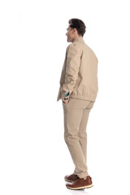 Bej ceketli mutlu bir genç adam el ele yürüyor ve beyaz arka planda gülümsüyor.