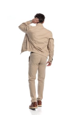 Kafası karışmış bej ceketli, kafası kaşınan ve beyaz arka planda yürürken sorunları düşünen genç bir adamın tüm vücudu.